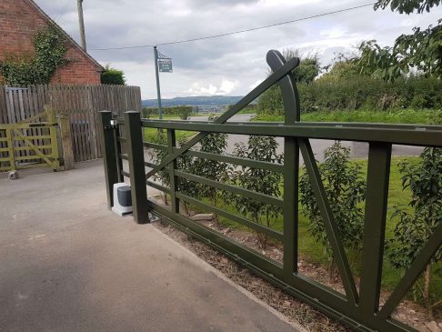 A 5 bar metal gate with automation at an angle, painted in dark green